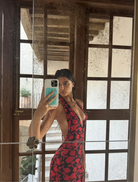 A woman wearing a red and black dress poses on a stone wall, highlighting her fashion choice in an outdoor setting.
