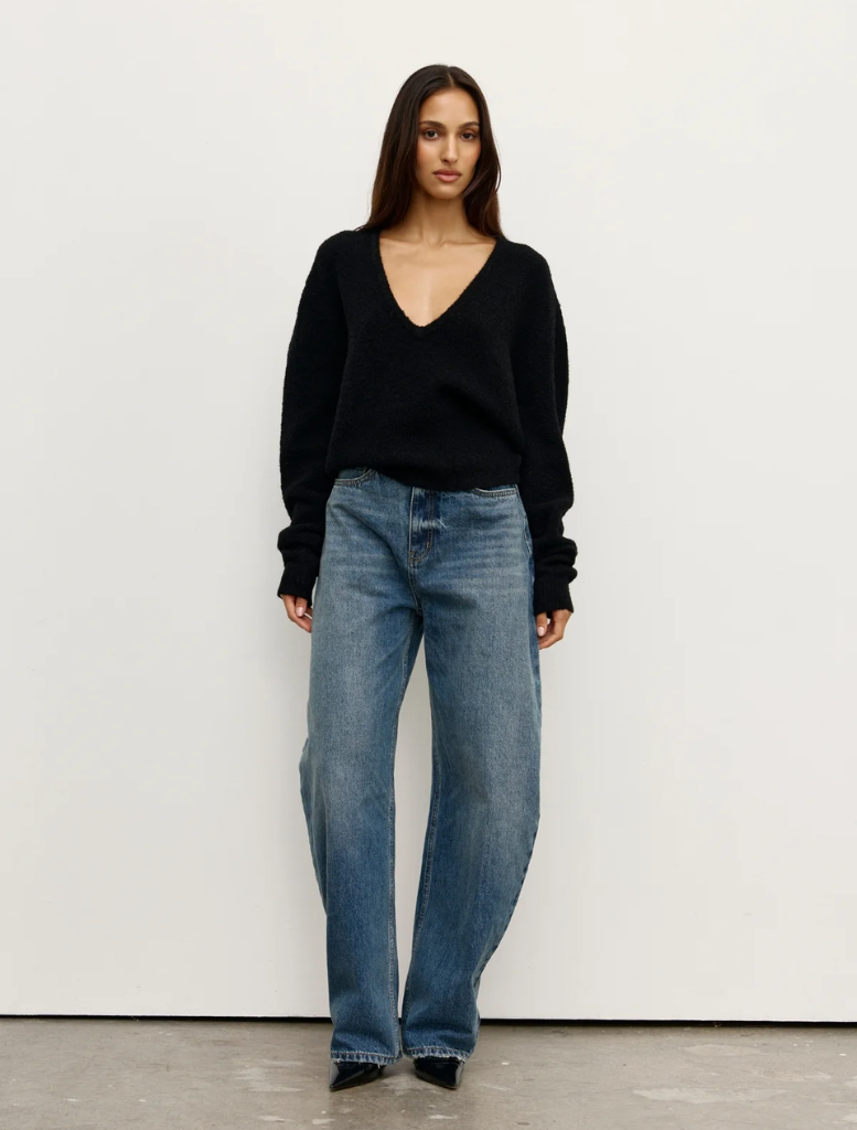 Black Sonia V-neck top displayed on a hanger, showcasing its elegant design and fabric texture.