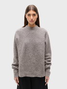 A beige grey crew neck sweater named Stella, hanging neatly for display.