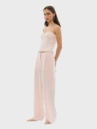 A woman models the Cleo Pant in pale pink, wearing a matching top and pants ensemble.