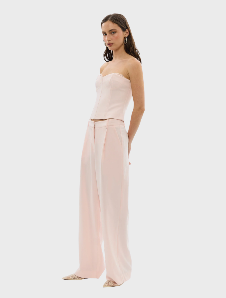 A woman models the Cleo Pant in pale pink, wearing a matching top and pants ensemble.
