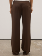 Chocolate Pietra Pant hanging on a hanger, illustrating its tailored design and rich color.