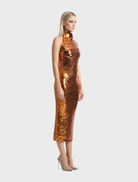A model displays The Area Dress, an orange gown embellished with copper sequins.