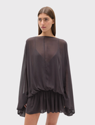 The Evariel Mini Dress in Truffle has a boat neckline, sheer draped upper, voluminous sleeves, and a flared mini skirt design.