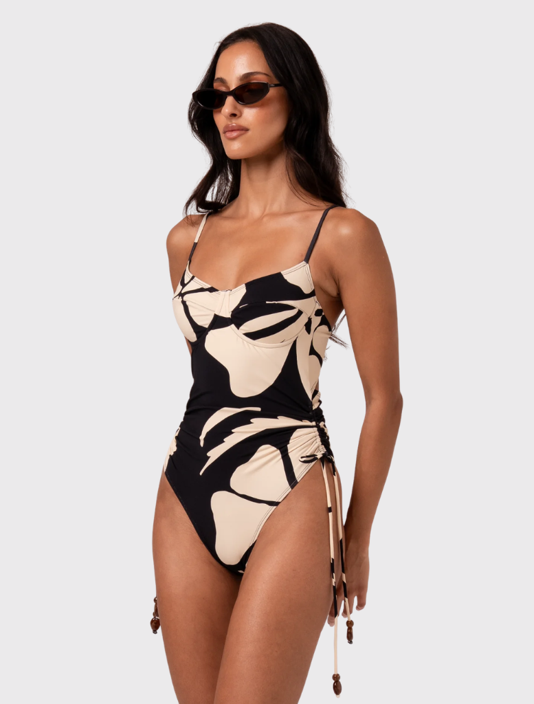 Elegant one-piece swimsuit with adjustable straps and side ties, finished in warm cream and black Botanica print for a chic look.