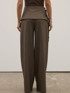 The model is dressed in a brown top and wide-legged Vela Pant, named Ash.