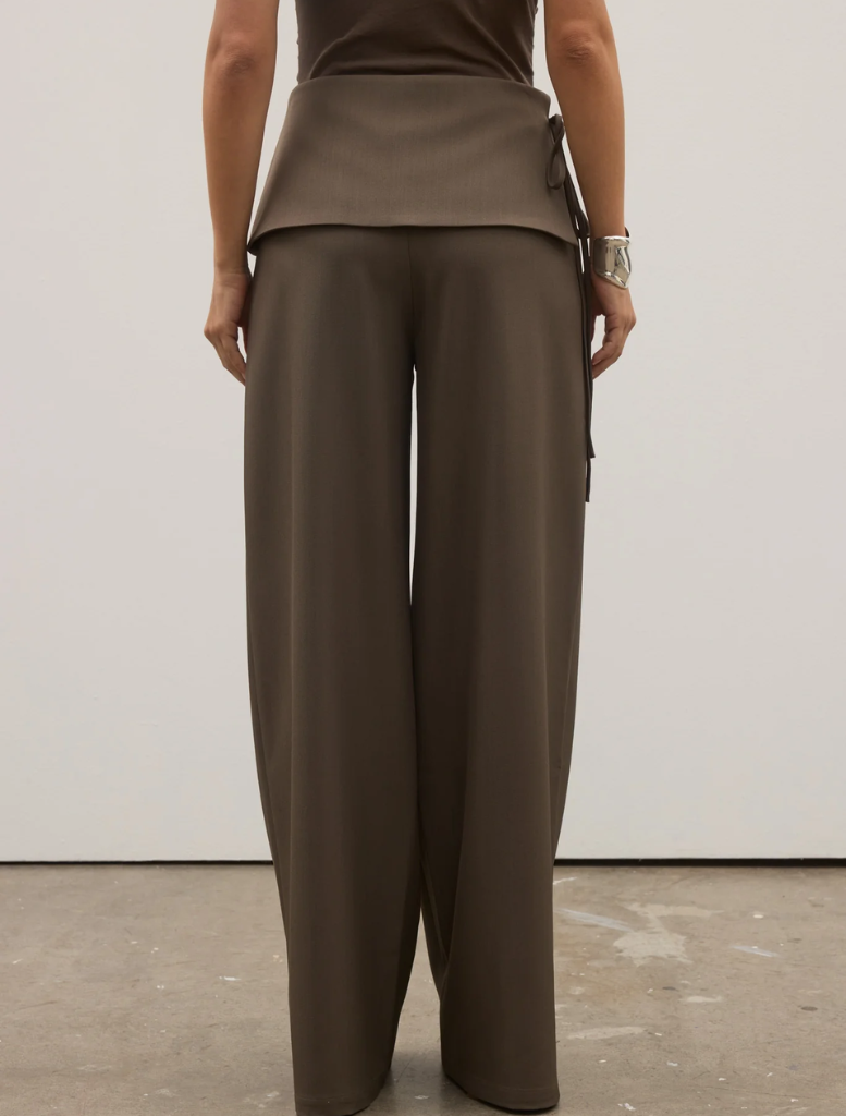 The model is dressed in a brown top and wide-legged Vela Pant, named Ash.