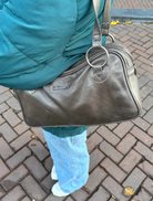 A brown leather handbag with two handles, elegantly positioned to showcase its design and texture.