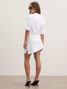 The model showcases a white t-shirt dress paired with stylish sunglasses, exuding a casual summer vibe.