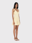 Butter yellow mini dress featuring ruffle trim, deep V neckline, open back, and asymmetrical hip panel.