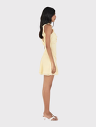 Stylish butter yellow mini dress with fitted design, deep V neckline, open back, and flared tiered skirt.