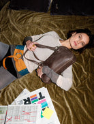 A woman wearing boots displays a multicolour Nuvola belt, along with a watch and various items in her hand.