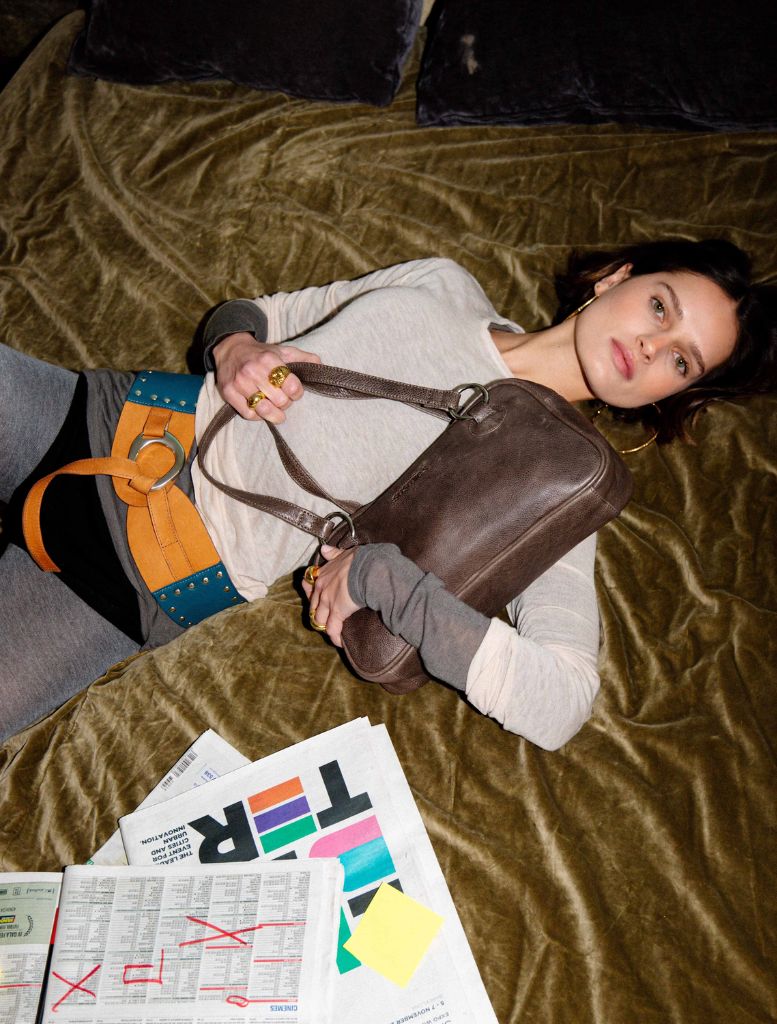 A woman wearing boots displays a multicolour Nuvola belt, along with a watch and various items in her hand.
