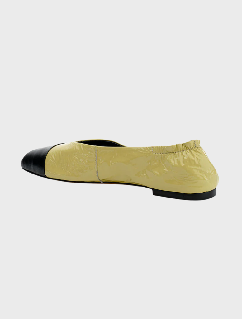 A pair of yellow and black flats featuring a black heel, made from pistachio oily crinkle leather.
