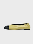 A pair of yellow and black flats featuring a black trim, made from crinkle leather with a pistachio oily finish.