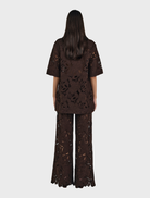 A woman in a black top and brown Lotus Lace pants, highlighting a chic fashion choice.